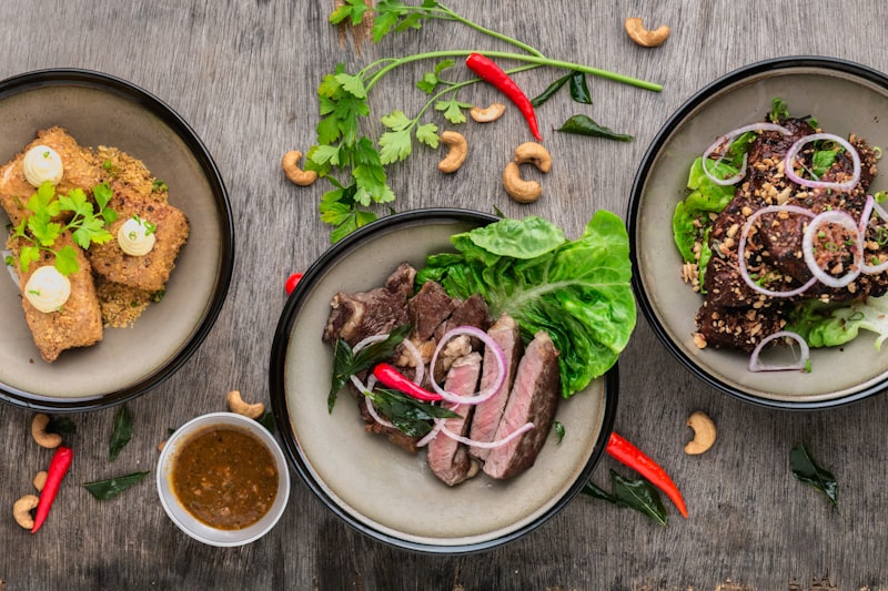 Cuisine Gourmet : Sélection de Plats de Viande et Poisson Plats de steak, poisson frit et côtes levées avec garnitures colorées sur table en bois rustique.