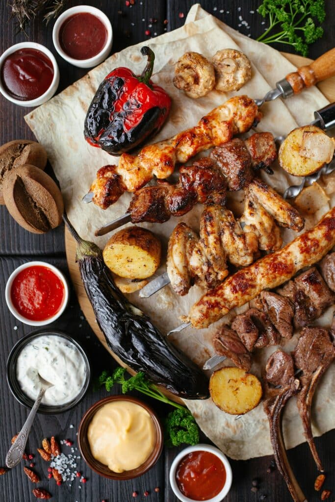 Plateau de grillades avec brochettes de viande, légumes rôtis, sauces variées et pain plat sur fond de bois.