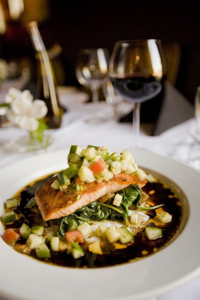 Saumon Poêlé et Salsa de Légumes au Vin Rouge Saumon poêlé sur lit d'épinards avec salsa de légumes, servi avec un verre de vin rouge dans un restaurant chic.