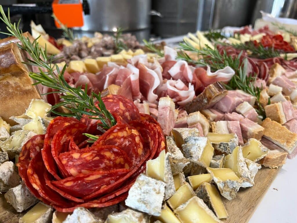Plateau de charcuterie et fromages : Idée apéritif gourmand Plateau de charcuterie artisanale avec rose de chorizo, prosciutto, fromages variés et branches de romarin frais.