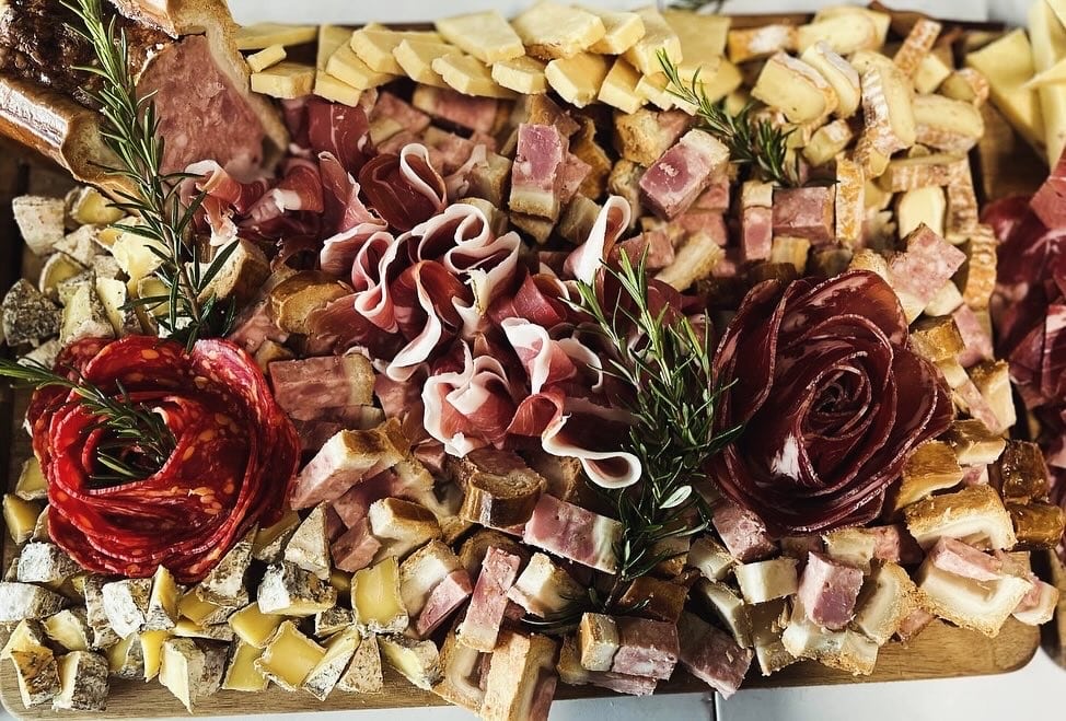 Plateau de Charcuterie et Fromage : Rosaces et Garnitures Plateau de charcuterie avec roses de salami, prosciutto, cubes de pâté, fromages variés et brins de romarin frais.